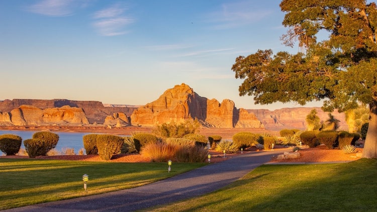 Sunlit desert cliffs above manicured lakeside lawn