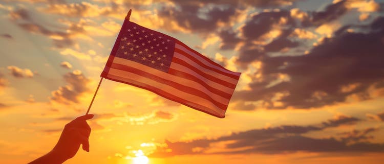 hand holding up a U.S. flag as the sun sets