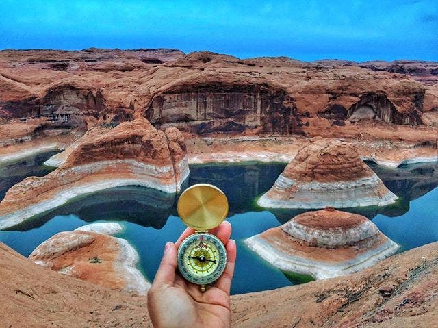 Scenic view overlooking the dramatic canyon landscape around Lake Powell with a hand holding a compass in the foreground